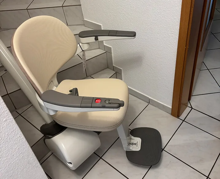 Treppenlift mit cremefarbenem Sitz auf Fliesentreppe